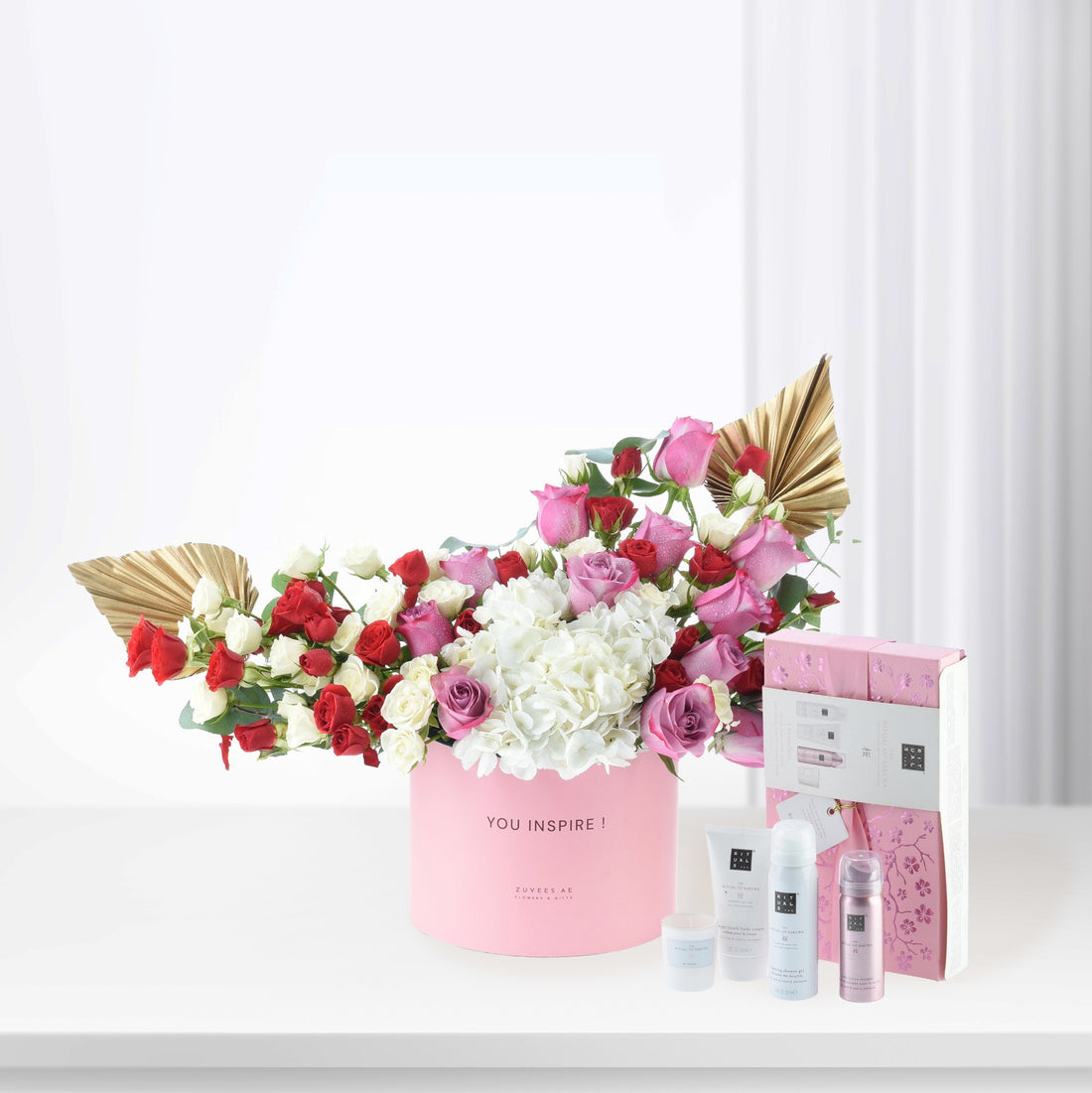 Pink floral arrangement with gold accents and luxury skincare set.