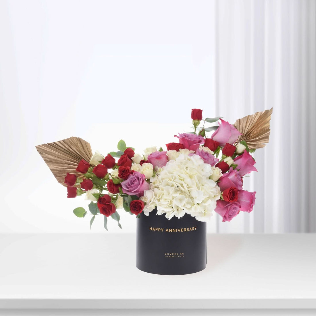 Elegant black box with "Happy Anniversary" text, holding vibrant red, pink, and white roses with gold leaf accents.