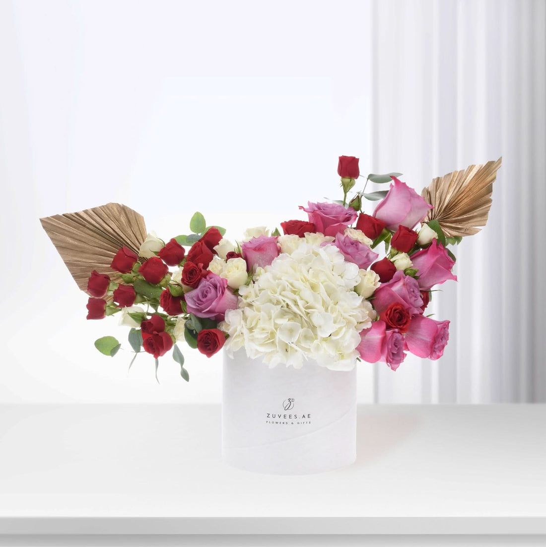 Elegant white box with red, pink, white roses, hydrangeas, gold leaves, Zuvees branding.