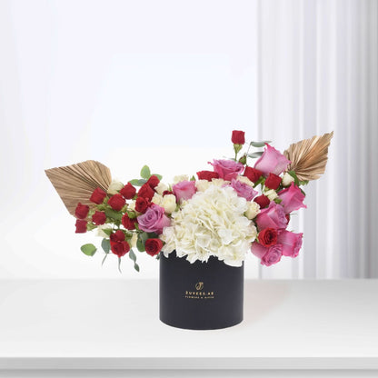 Elegant black box holds vibrant red, pink roses and white hydrangeas, accented with gold leaves.