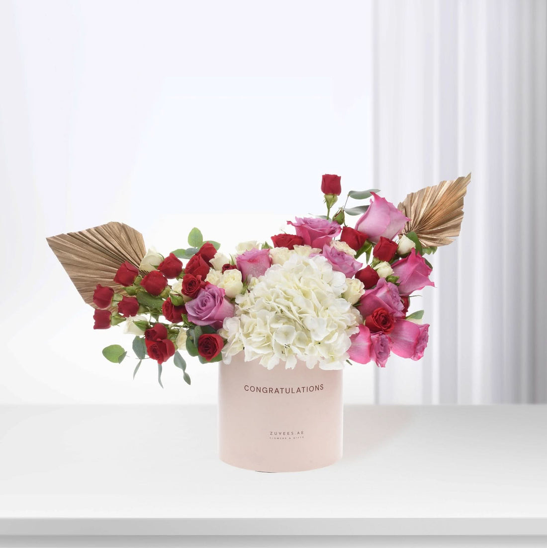 Pink "Congratulations" vase with red, pink, white roses, hydrangeas, gold palm leaves, elegant gift arrangement.
