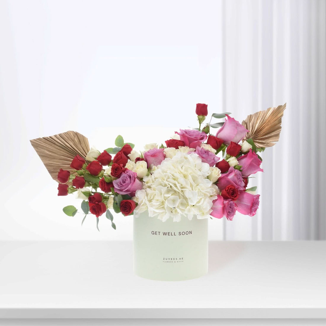Pastel green vase holds vibrant red, pink, and white roses with gold fan accents.
