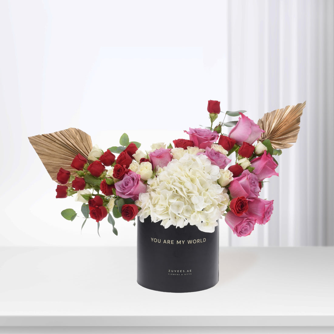 Black vase with "You Are My World" holds vibrant red, pink, and white roses and hydrangeas, accented by gold leaf fans.