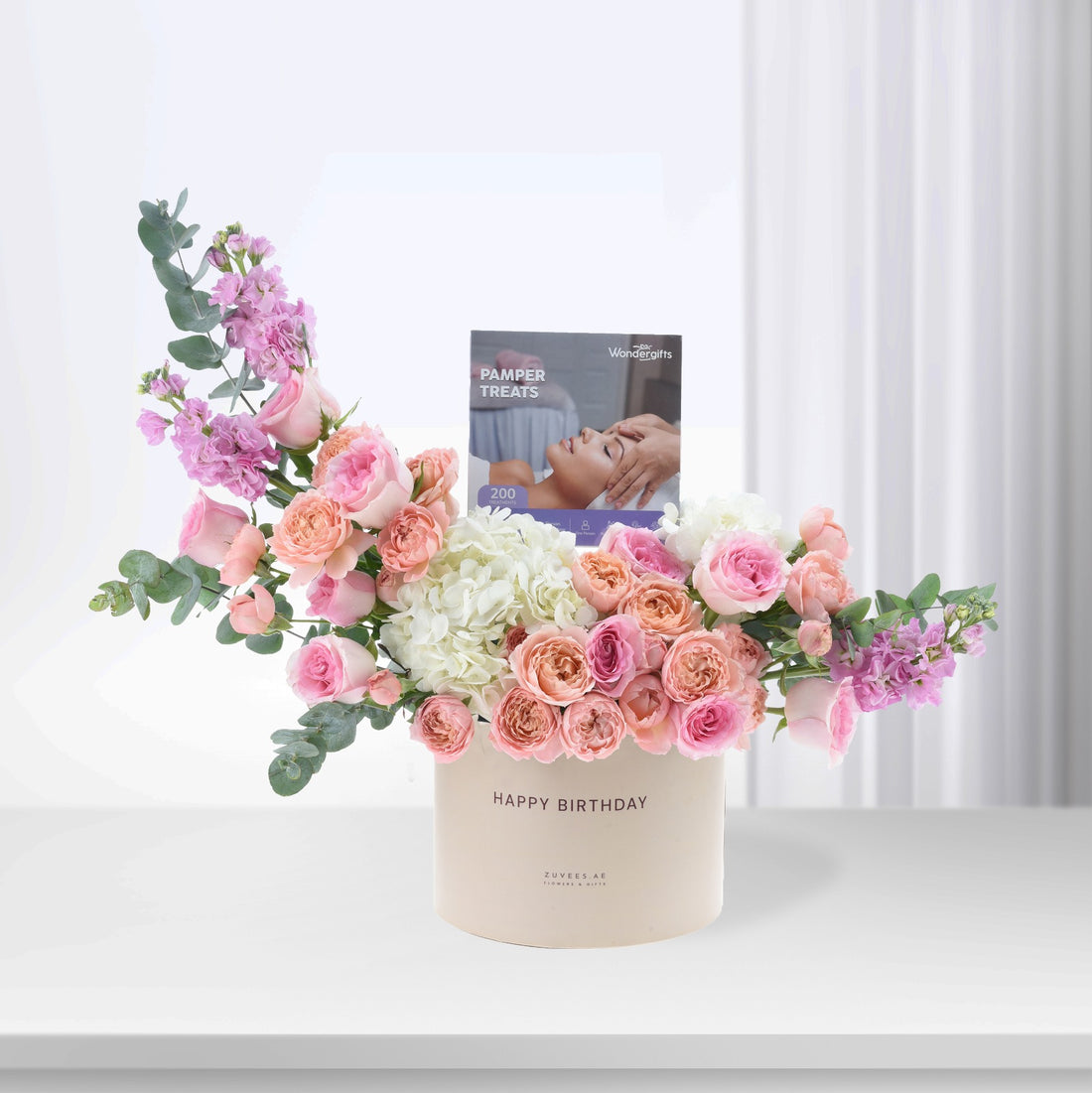 Pastel pink roses, hydrangeas, and eucalyptus in cream box with "Happy Birthday" and pamper treats booklet.