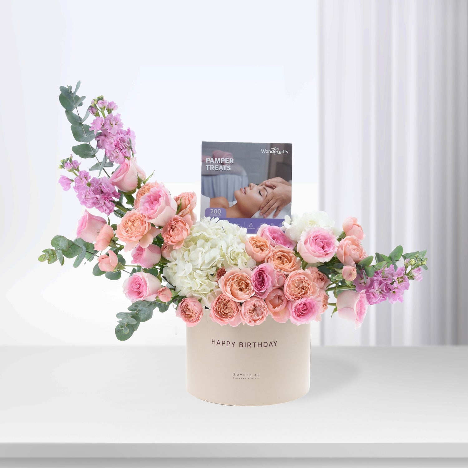 Pastel pink roses, hydrangeas, and eucalyptus in cream box with "Happy Birthday" and pamper treats booklet.