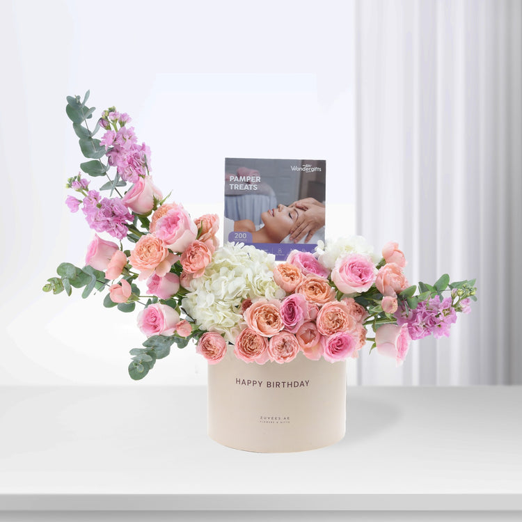 Pastel pink roses, hydrangeas, and eucalyptus in cream box with "Happy Birthday" and pamper treats booklet.