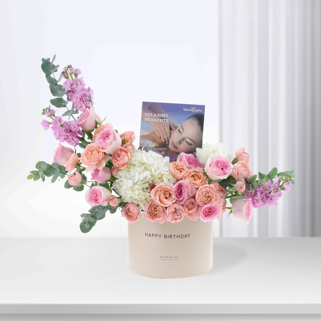 Pastel pink roses, hydrangeas, and eucalyptus in cream box with "Happy Birthday" and massage voucher.
