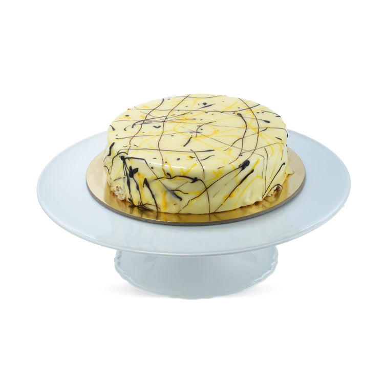 Creamy yellow cake with chocolate and yellow drizzle, elegantly displayed on a light blue cake stand.