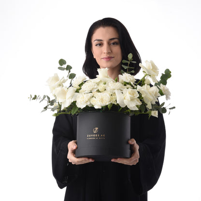 Elegant woman holds black box overflowing with pristine white roses and eucalyptus.