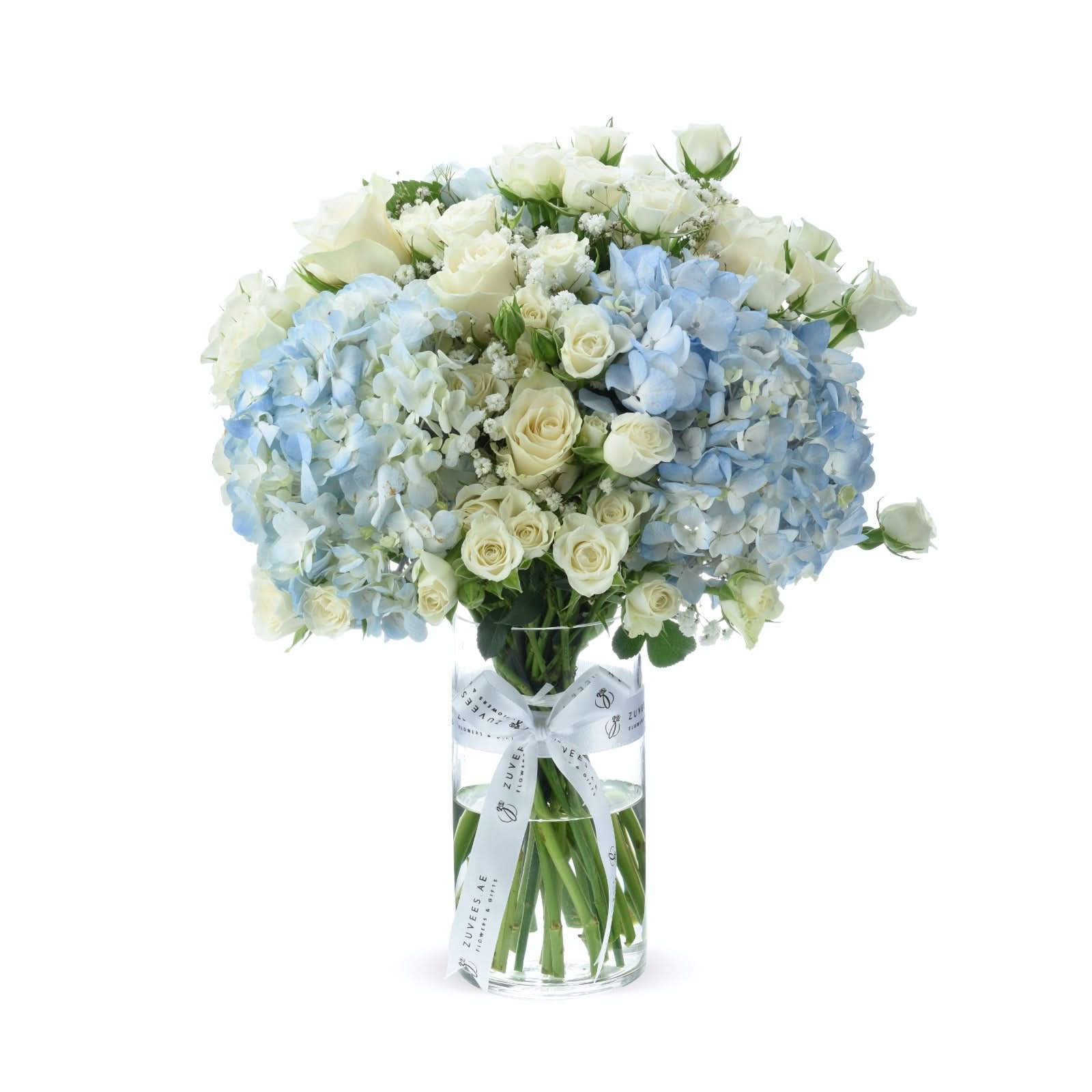 Elegant blue hydrangeas and white roses in clear vase with branded ribbon.