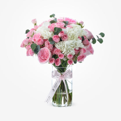 Pink roses and white hydrangeas in clear vase with branded ribbon.