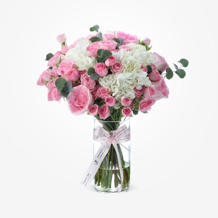 Pink roses and white hydrangeas in clear vase with branded ribbon.