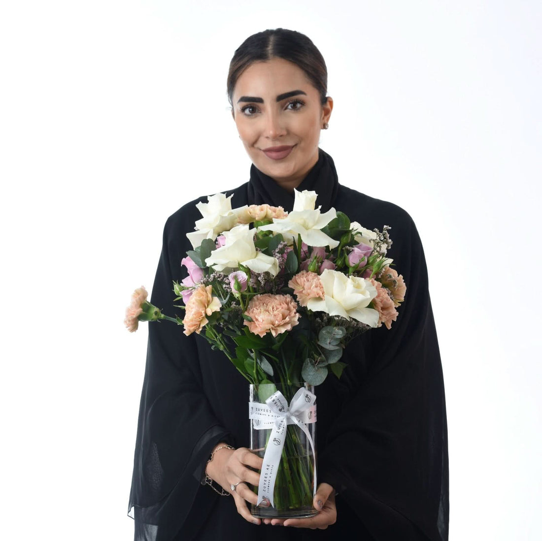Elegant woman holds pastel rose and carnation bouquet in branded glass vase.