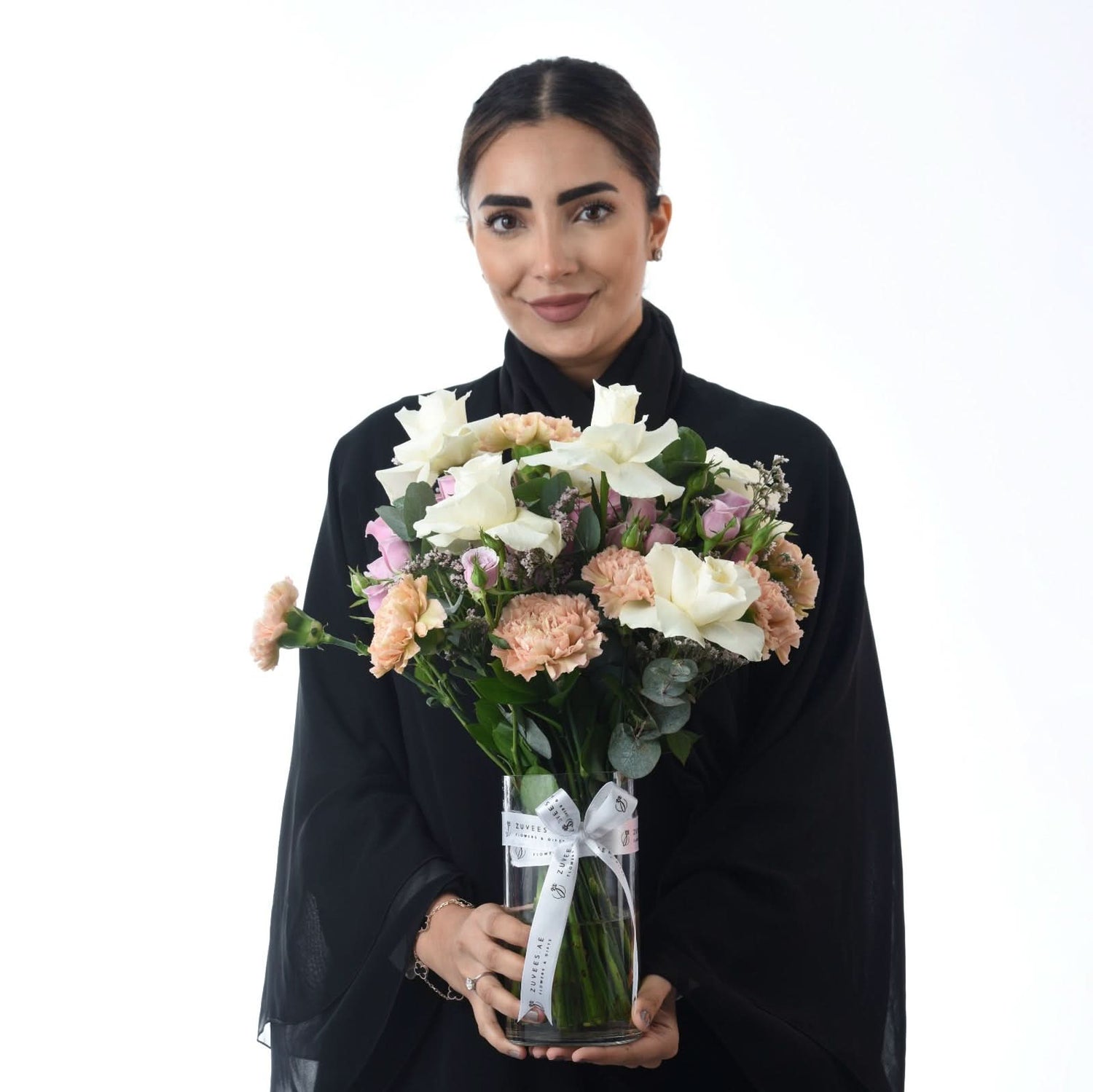 Elegant woman holds pastel rose and carnation bouquet in branded glass vase.