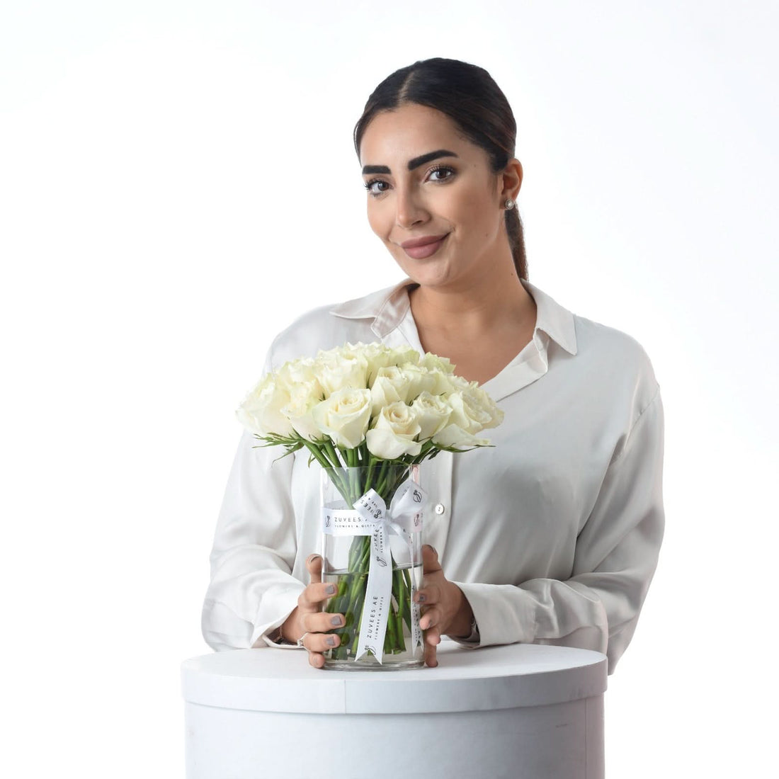 Woman holds elegant white rose bouquet in branded glass vase against clean white background.