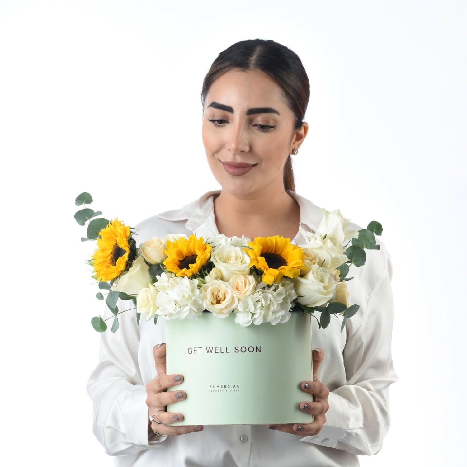 Woman holds mint box with sunflowers and white roses saying “Get Well Soon.”