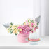 Pink floral arrangement with silver fan accents beside white-frosted cake.
