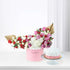 Pink box holds red, pink, white roses and hydrangeas, beside cake with rose icing.