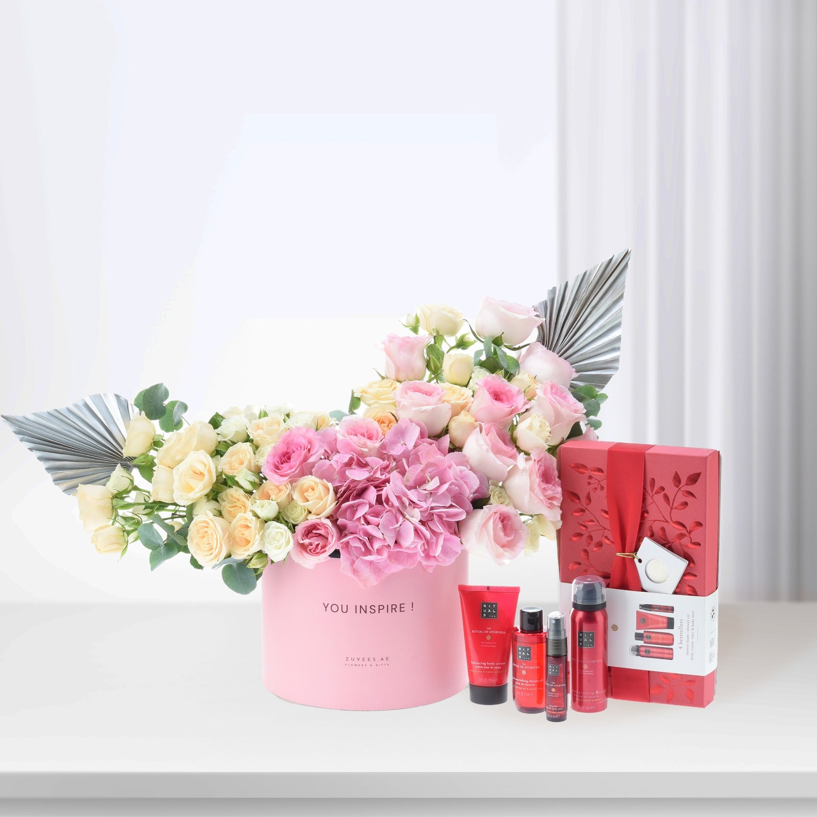 Pink floral arrangement with silver accents beside red Rituals gift set.