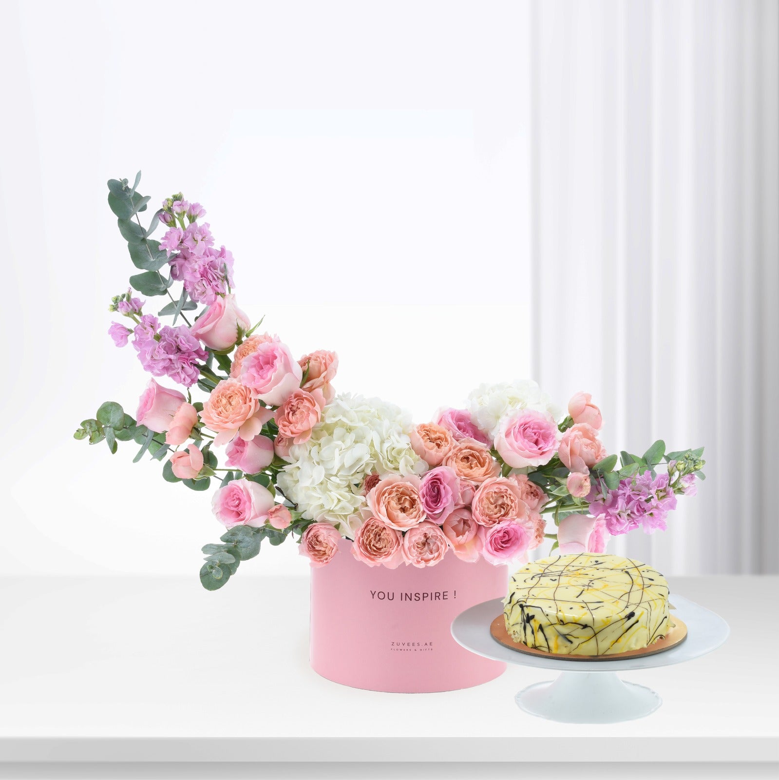 Pink floral arrangement with cake beside, elegant gift set.