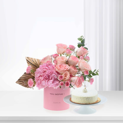 Pink roses and hydrangeas in branded box beside coconut cake.
