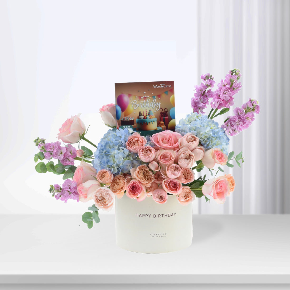 Pastel pink roses, blue hydrangeas, and purple blooms in white "Happy Birthday" box.