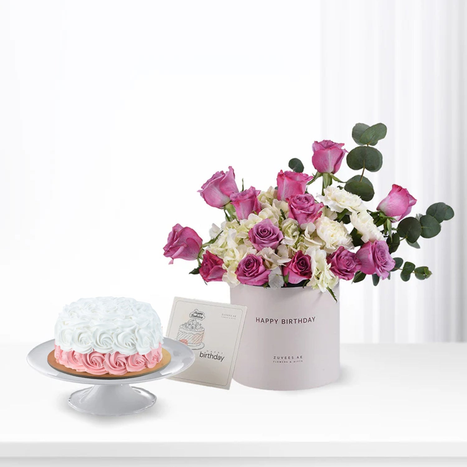 Pink roses and white hydrangeas in box beside ombre cake.