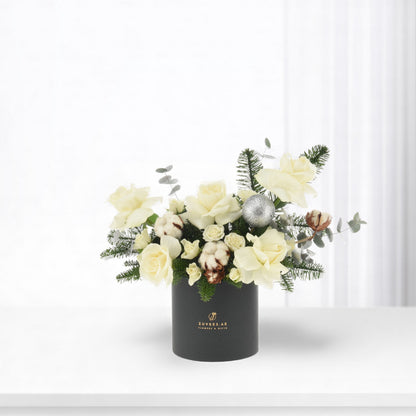 Elegant white rose bouquet in matte black vase with silver ornament and greenery.