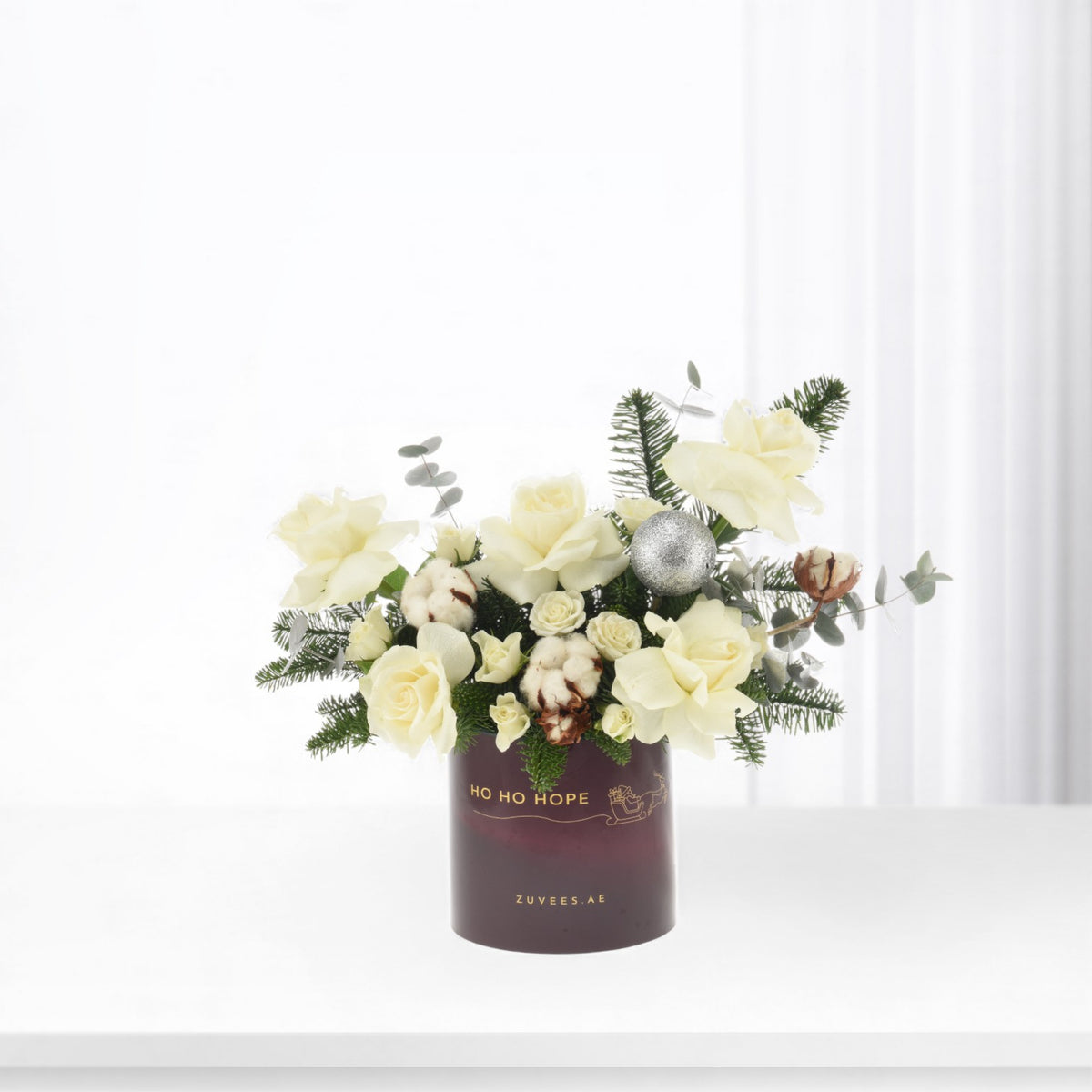Cream roses, cotton, pine, silver bauble in burgundy "HO HO HOPE" vase, festive elegance.