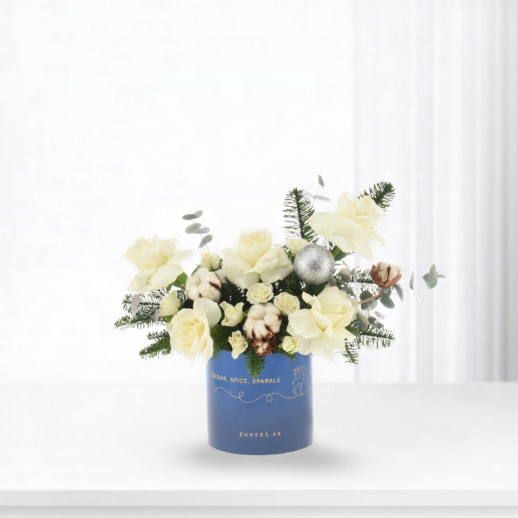 White roses, cotton, and evergreens in blue vase with silver ornament.