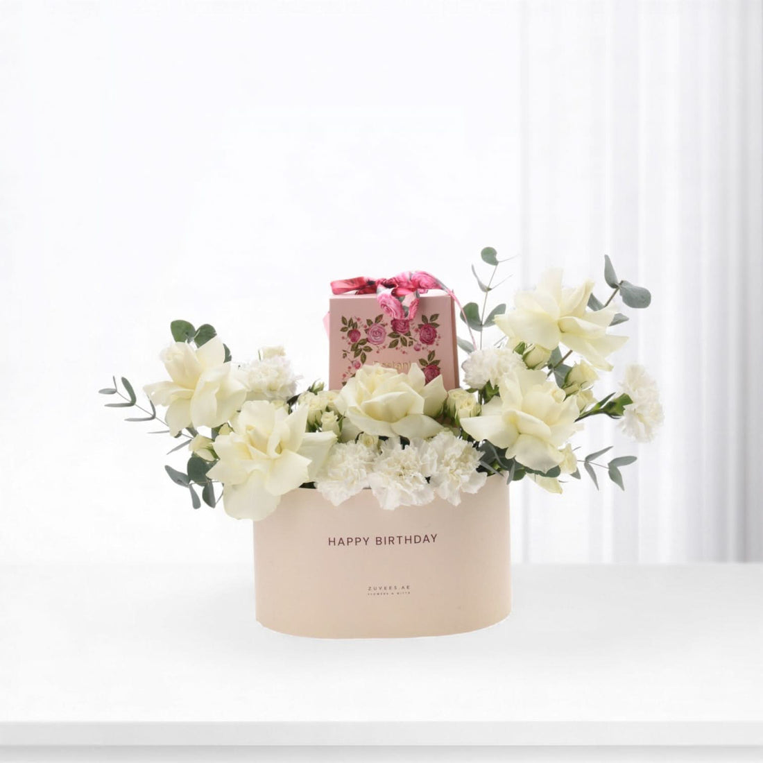 Soft pink box holds creamy white roses, carnations, and eucalyptus for birthday celebration.