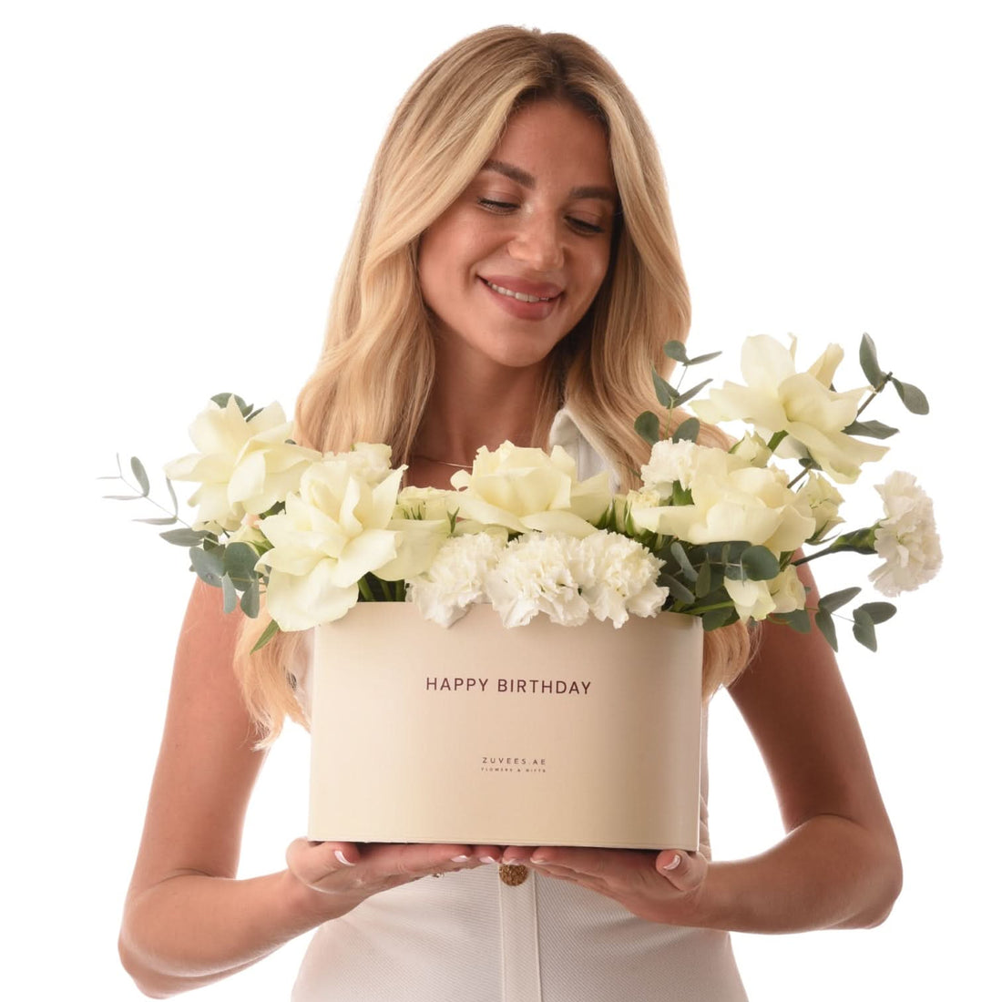 Blonde woman holds elegant cream box with white roses, carnations, eucalyptus, "Happy Birthday" text.