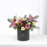 Elegant black vase holds pink, yellow roses, pine, pinecones, and red ornaments.