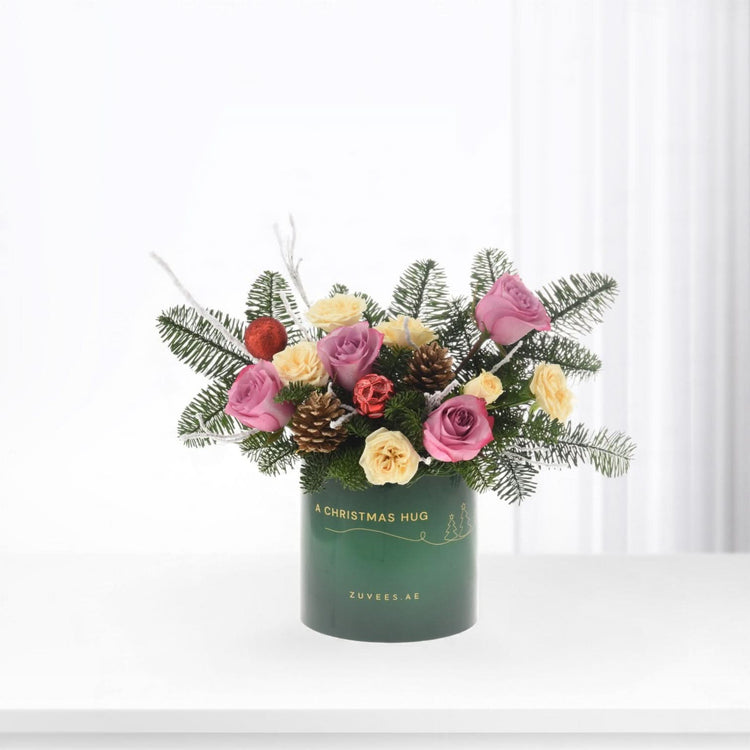 Green vase holds pink, yellow roses, pine, pinecones, red ornaments—festive holiday arrangement.