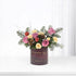 Purple vase holds pink, yellow roses, pine, pinecones, red ornaments, festive "Ho Ho Hope" text.