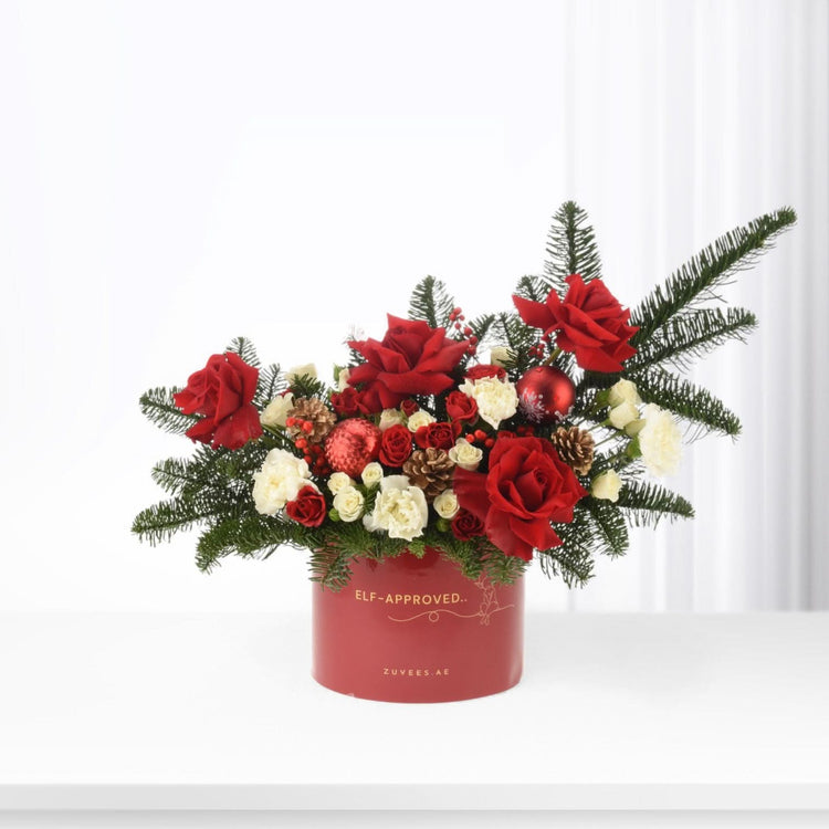 Vibrant red roses, white blooms, pine, and ornaments in festive red box.