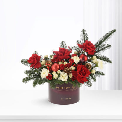 Vibrant red roses, white blooms, pine, and ornaments in festive deep purple box.