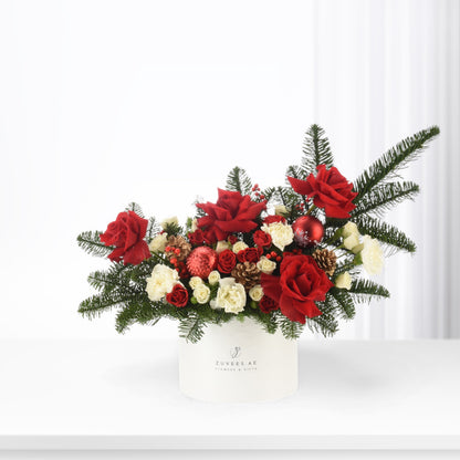 Vibrant red roses, white carnations, pine, pinecones, and red ornaments in white box.