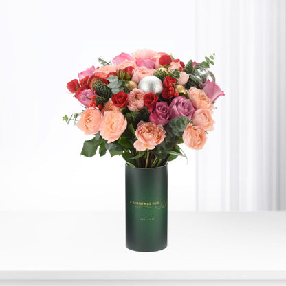 Vibrant pink, red roses and berries in festive green vase.