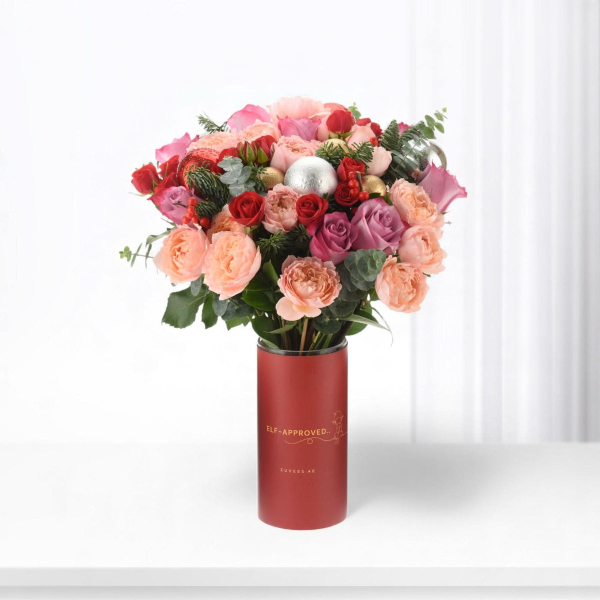 Vibrant red, pink, and gold roses in festive red cylinder vase with "Elf-Approved" text.