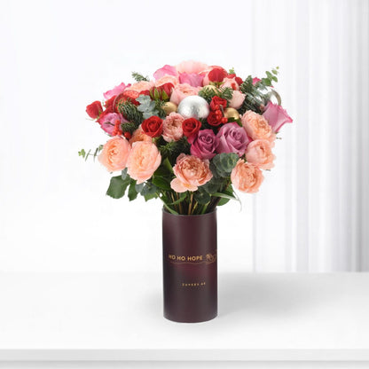 Vibrant pink, red, and purple roses in festive holiday-themed vase with "Ho Ho Hope" text.