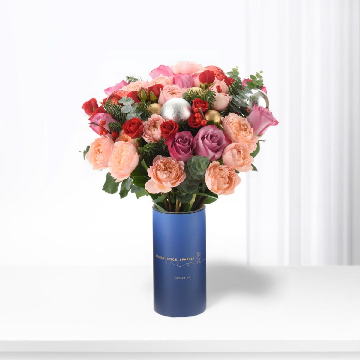 Vibrant pink, red, and purple roses in festive blue cylinder vase with gold accents.