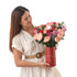 Woman holds festive red cylinder bouquet with roses, berries, and silver ornaments.