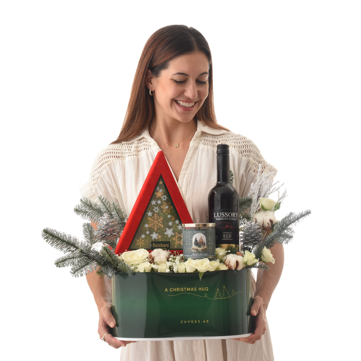 Woman smiles holding festive green gift basket with wine, candles, and white roses.