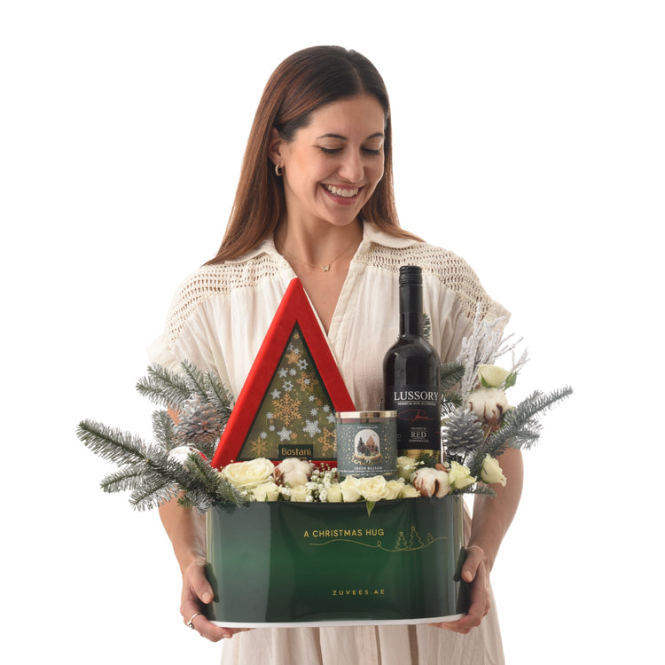 Woman smiles holding festive green gift basket with wine, candles, and white roses.
