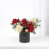 Elegant black vase holds vibrant red and cream roses, pine, cotton, and a shiny red ornament.