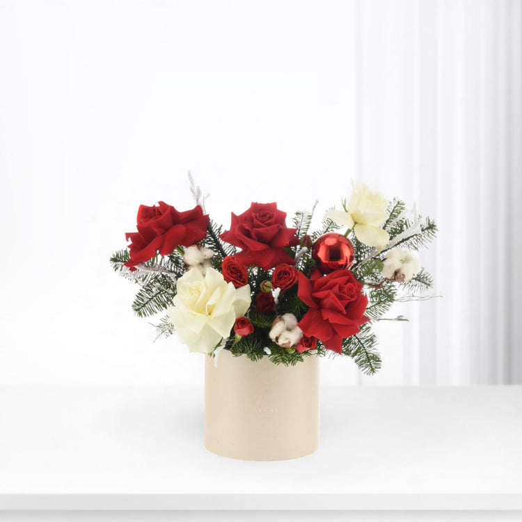 Red and cream roses, fir, cotton, and ornament in beige vase.