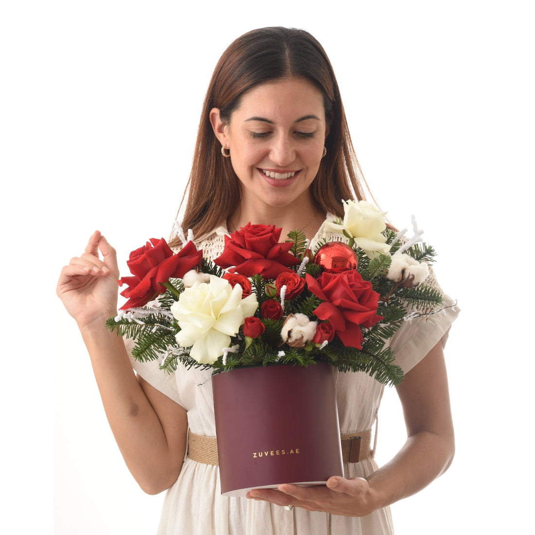 Woman smiles holding burgundy box with red and white roses, pine, cotton, and red ornament.