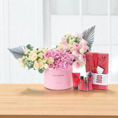 Pink floral arrangement with metallic fans, paired with red skincare set on wooden surface.
