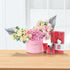 Pink floral arrangement with metallic fans, paired with red skincare set on wooden surface.